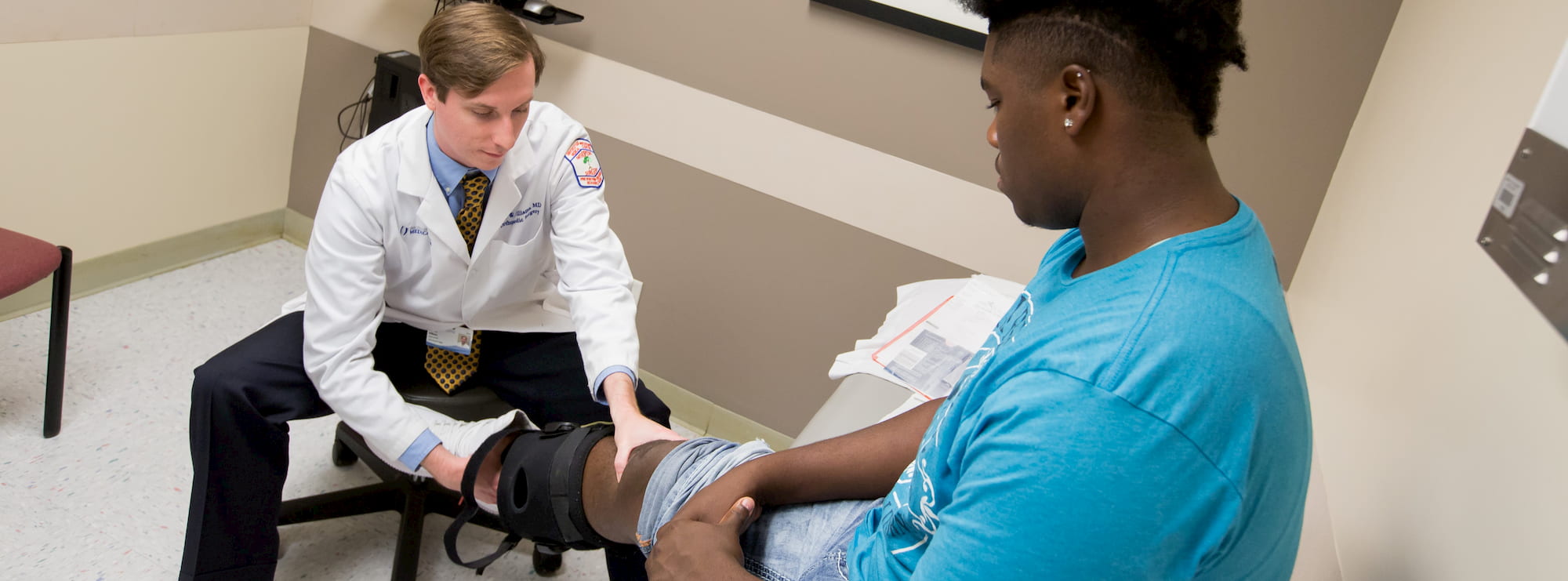 Orthopedic physician examines an injured knee in a brace. Orthopedic physician examines an injured knee in a brace.